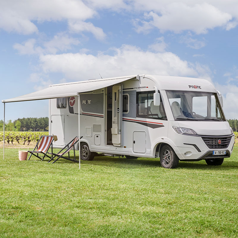 Camping-car intégral Pilote à l'étape, store banne déplié, sur une étendue d'herbe.