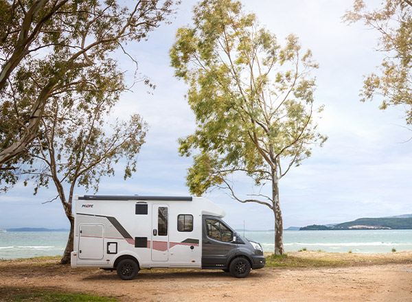 Camping-car profilé étroit Pilote sur un chemin à l'arrêt, en bord de mer, le ciel gris et menaçant en arrière-plan.