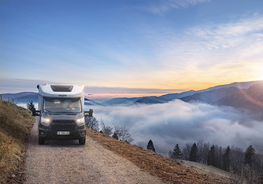 Camping-car profilé étroit Pilote sur un chemin caillouteux, au dessus d'une mer de nuages.