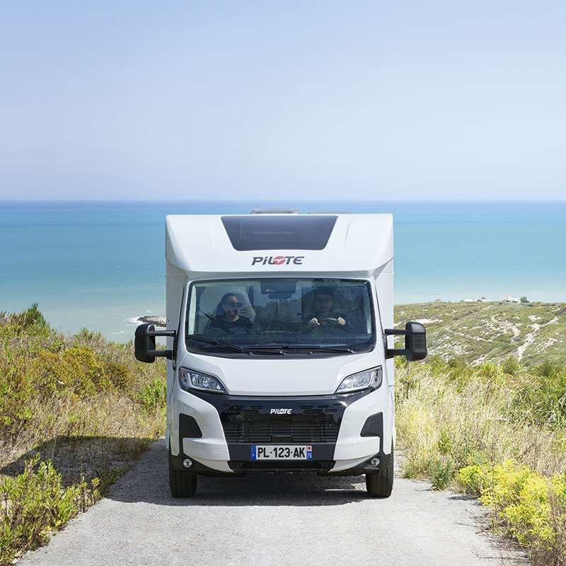 Camping-car profilé Pilote sur une route de Bretagne, la mer en arrière plan.