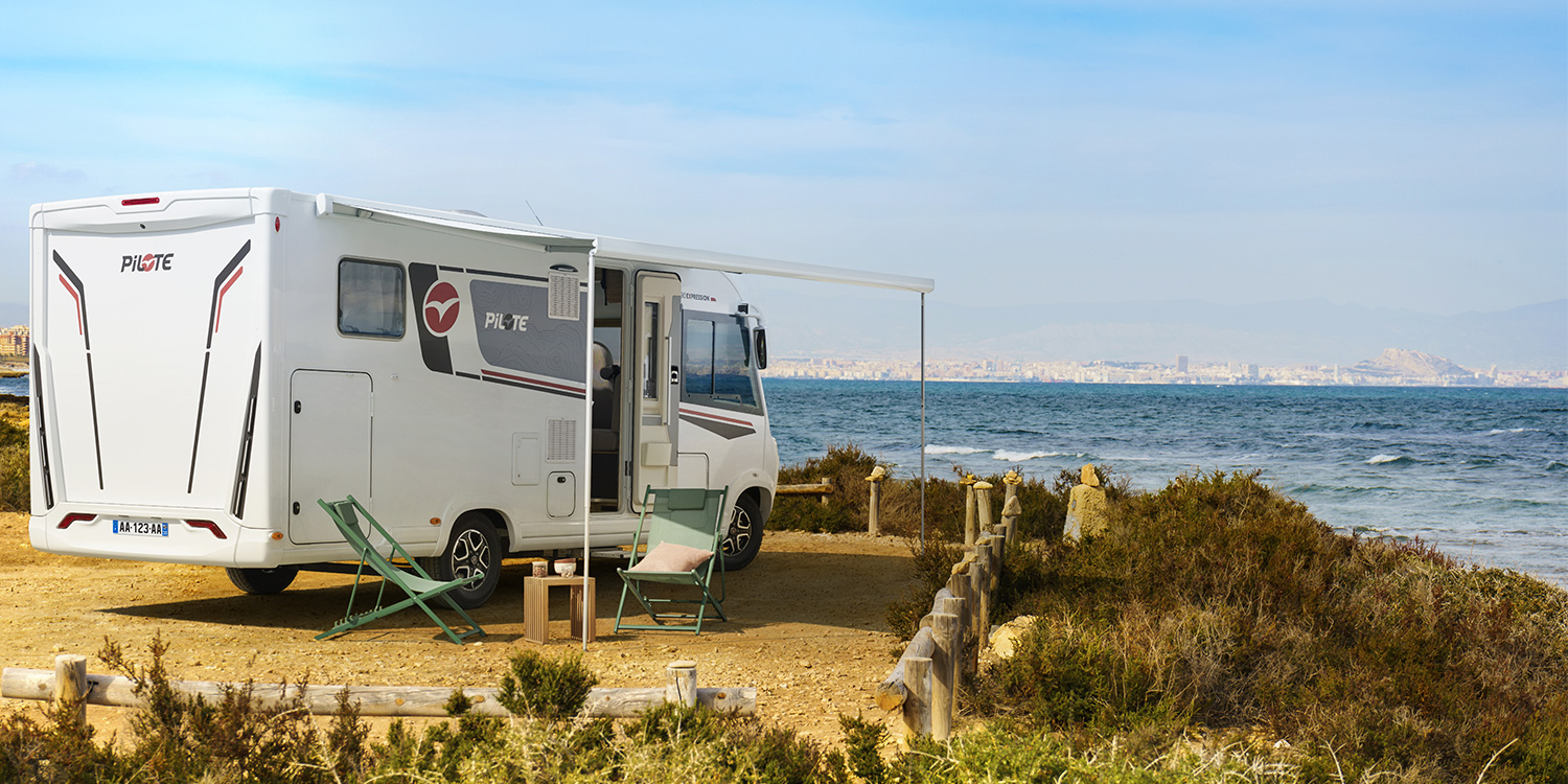 Camping-car intégral Pilote à l'étape, store banne déplié et chaises longues sorties, pour profiter du soleil et de la vue sur mer.