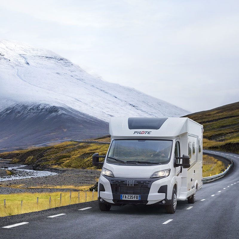 Camping-car profilé Pilote roulant sur une route d'Islande, entre steppes et montagnes enneigées au loin.