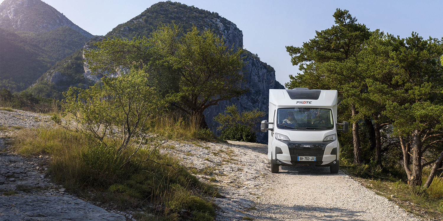 Camping-car profilé Pilote roulant sur une chemin caillouteux au milieu de la végétation.